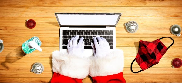 Santa Clause hands using a laptop with a facemask and hand sanitiser on table