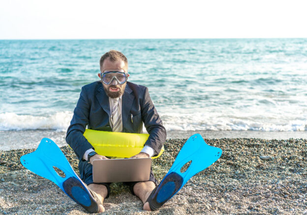 man sitting at the beach with his laptop and checking email wearing swimming fins and swimming goggles